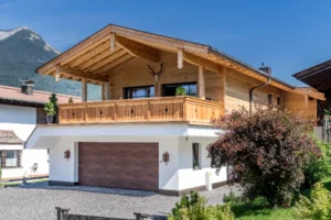 Holz-Wohnbau-Projekt in Ehrwald – zweigeschossiges Einfamilienhaus mit Holzverkleidung im Obergeschoss, großem Balkon und Garage im Erdgeschoss vor Bergkulisse